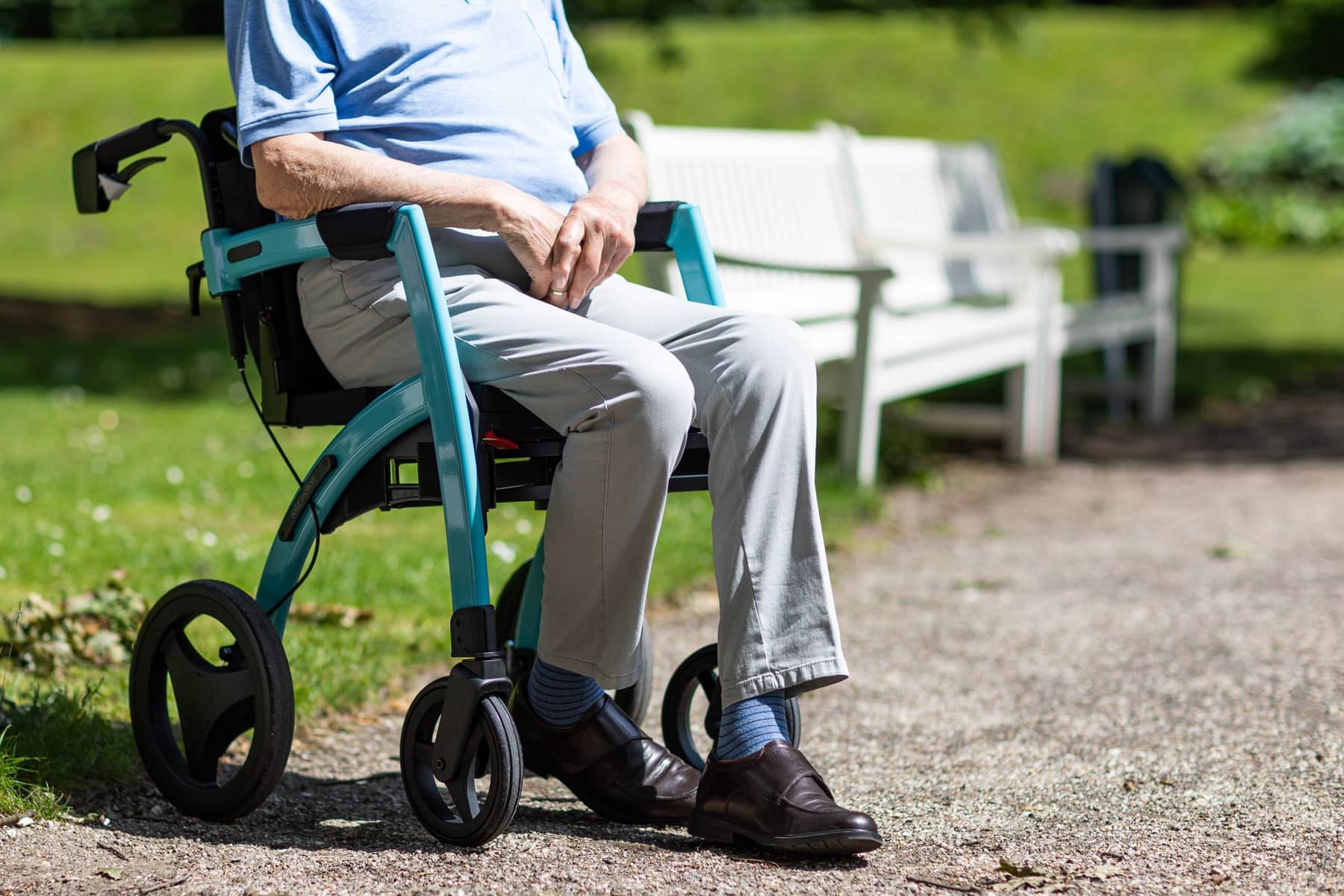 An older adult resting on a rollator on a sunny park path